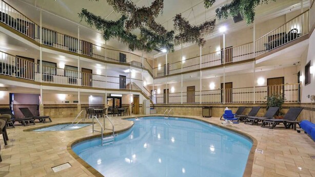 A multi-level indoor pool with a central swimming area, multiple balconies, and lounge chairs. - Studio 6 Minot, ND (Minot)