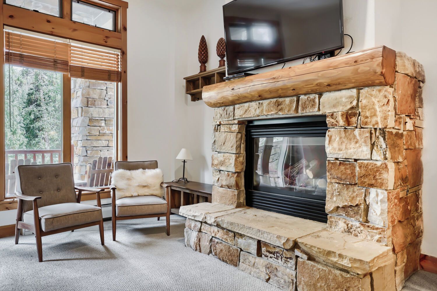 Una chimenea de piedra con un televisor encima, un sillón con una manta de piel y una ventana con persianas.