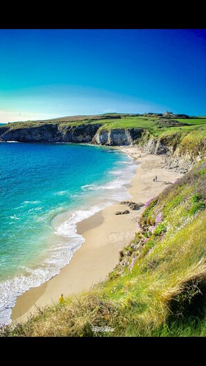 A coastal landscape with a sandy beach, cliffs, and a clear blue sea.