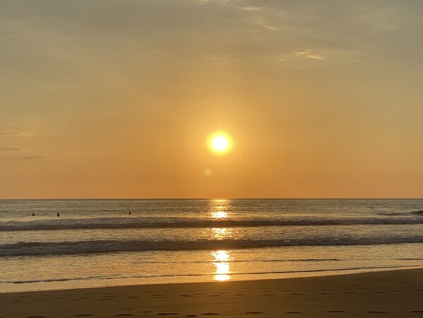 Una playa con el sol poniéndose sobre el océano, creando un reflejo en el agua.