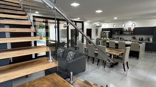 Una cocina moderna con comedor, una escalera con barandillas de cristal y una sala de estar con sofá y mesa de centro.