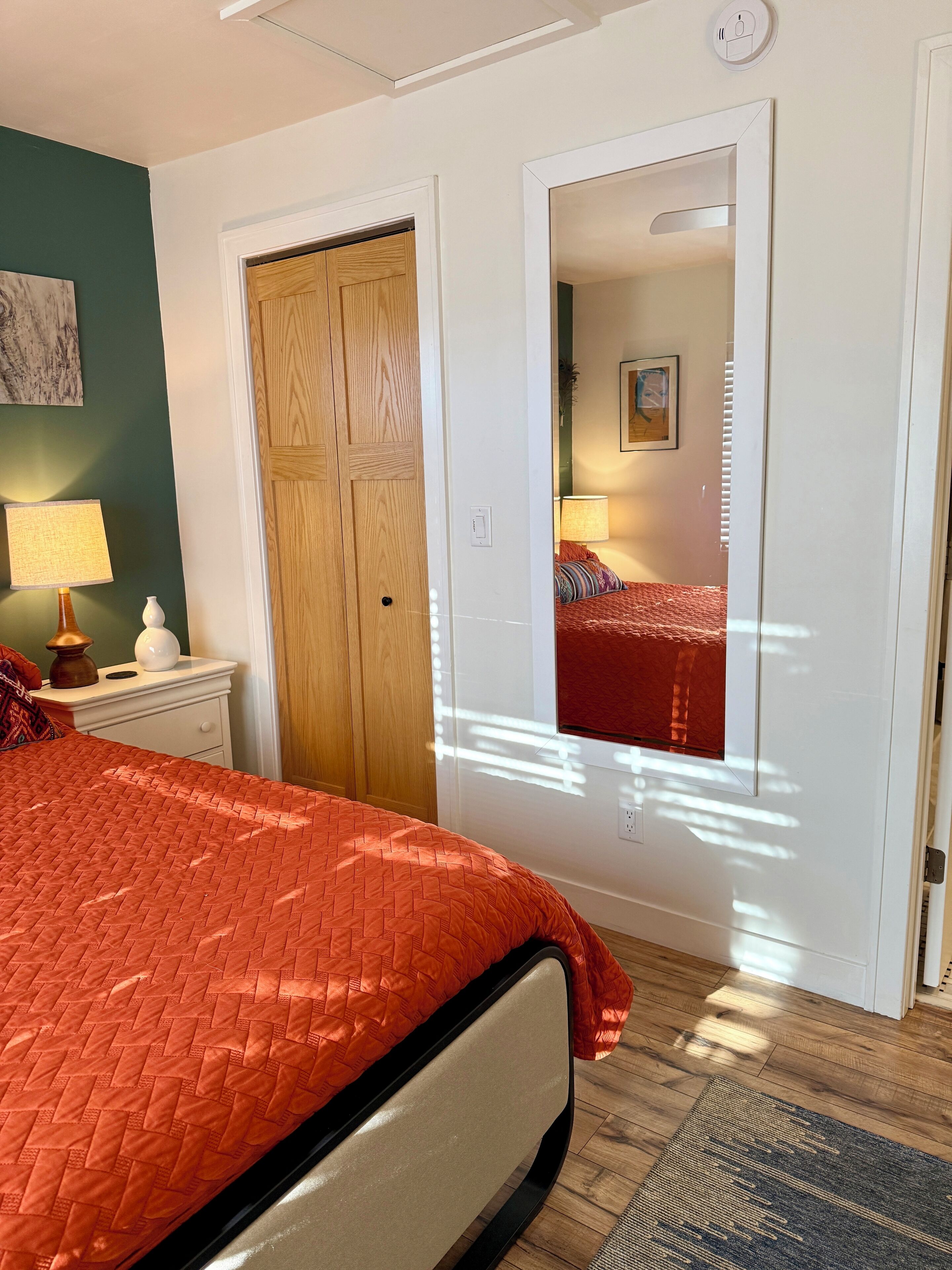 A bedroom with a bed, a nightstand, a mirror, and a door.