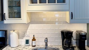 Una cocina con armarios blancos, encimera de mármol, pileta de acero inoxidable, cafetera y dispensador de toallas de papel.