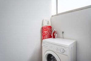 Laundry room with a front-loading washing machine, ironing board, and iron.