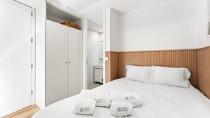 A hotel room with a wooden headboard, a bed with white linens, a closet with white doors, and a bathroom visible in the background. - GuestReady - Easygoing Pool to River (Vila Nova de Gaia)
