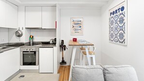 A compact kitchen with white cabinets, a stove, and a sink. There is a small dining area with a table and chairs, and a framed picture on the wall. - GuestReady - Easygoing Pool to River (Vila Nova de Gaia)