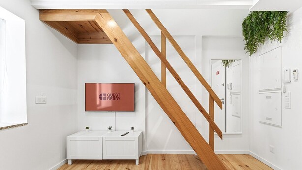 A modern hotel room with a wooden staircase, a mounted television, a white cabinet, and a plant. - GuestReady - Easygoing Pool to River (Vila Nova de Gaia)