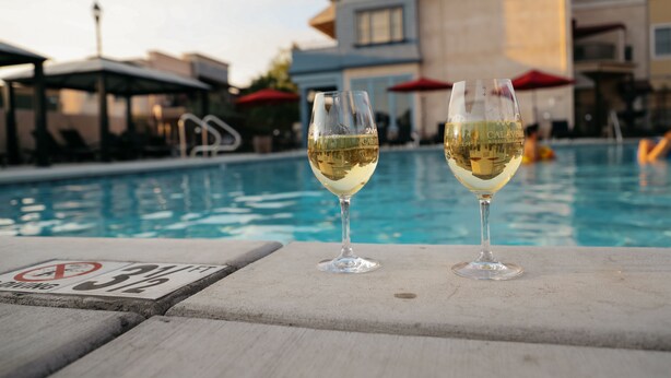 Deux verres de vin blanc sur une table au bord de la piscine, avec un panneau indiquant qu’il est interdit de plonger.