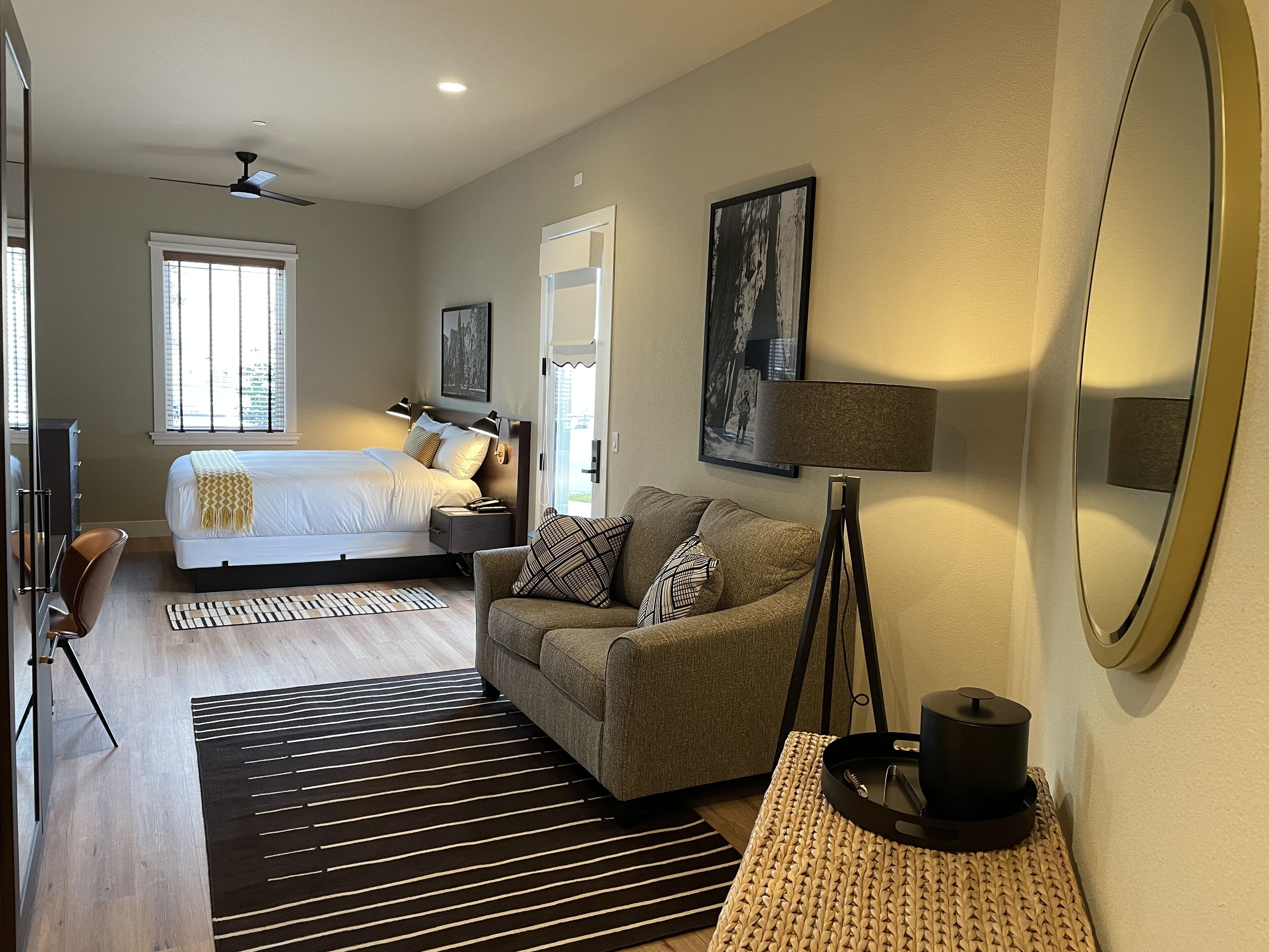 A modern bedroom with a bed, bedside tables, a standing lamp, a sofa, and a large mirror.