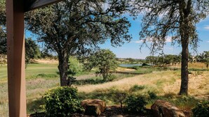 Une vue depuis un espace abrité donnant sur un terrain de golf, avec des arbres et une étendue d’eau en arrière-plan.