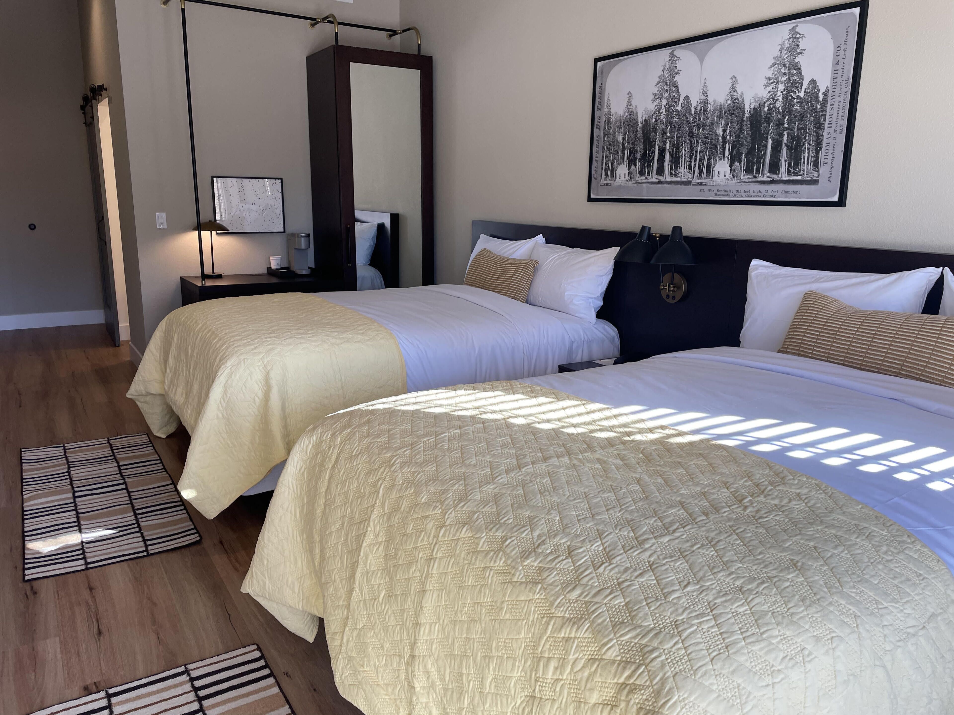 Habitación de hotel con dos camas, un espejo grande, un cuadro enmarcado en la pared y una mesita de noche con una lámpara.