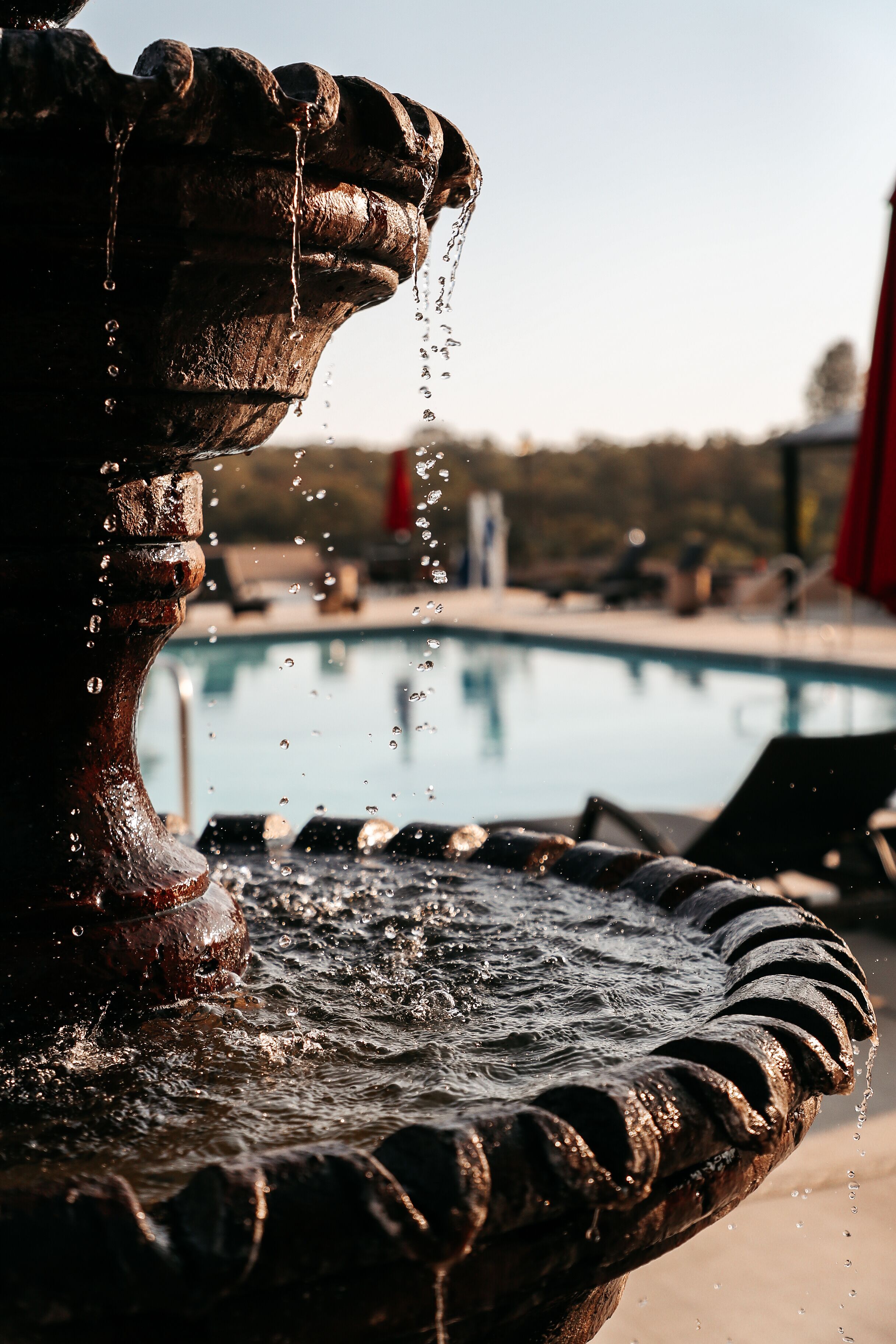 Primer plano de una fuente de agua, con una piscina al fondo.