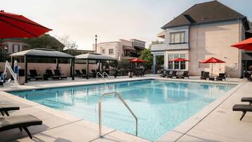 A swimming pool with lounge chairs and umbrellas, surrounded by buildings.