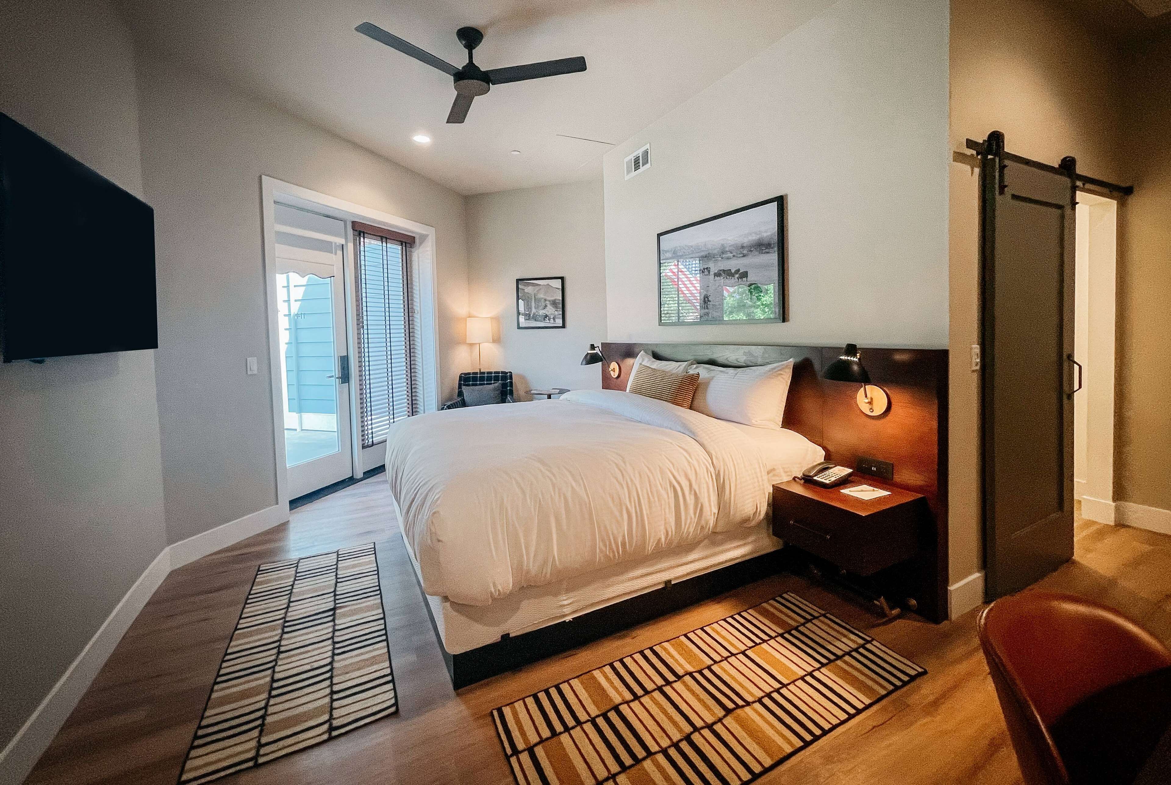A bedroom with a bed, bedside table, lamp, and a ceiling fan.