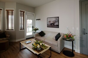 A living room with a sofa, a coffee table with flowers, a framed picture on the wall, and a door. - Gateway Hotel, Trademark Collection by Wyndham (Copperopolis)