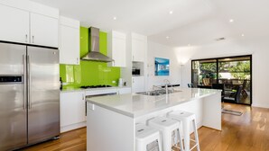 A modern kitchen with a stainless steel refrigerator, a gas stove, and a large island with bar stools. - Swainson on Lexington (Henley Beach South)
