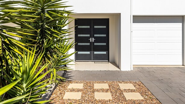 A modern building with a black door, a garage, and a paved entrance area with pebbles. - Swainson on Lexington (Henley Beach South)