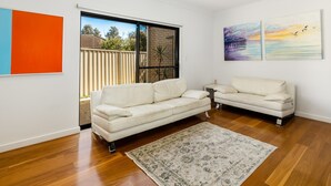 A modern living room with a white sofa, a patterned rug, and two wall-mounted paintings. - Swainson on Lexington (Henley Beach South)