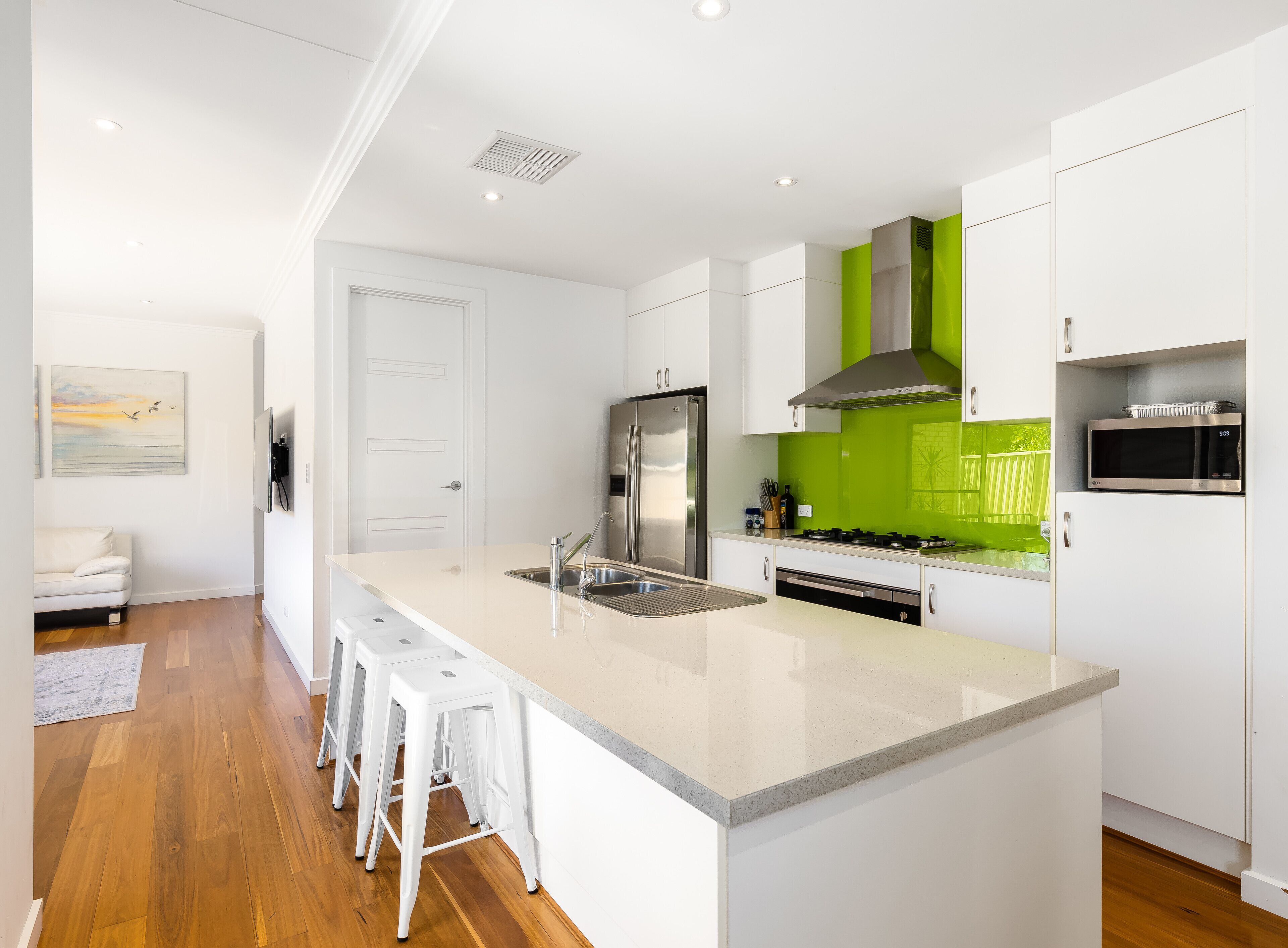 A modern kitchen with a central island, stainless steel appliances, and a green backsplash.