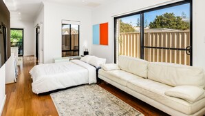 A modern bedroom with a large window, a bed, a sofa, and a desk. - Swainson on Lexington (Henley Beach South)