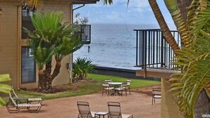 A patio area with outdoor seating, a view of the ocean, and palm trees.