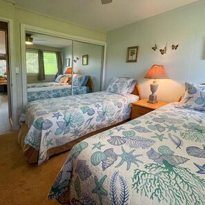 Une chambre avec deux lits, chacun recouvert d’une couvre-lit à motifs floraux, une table de chevet avec une lampe et un miroir au mur.