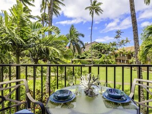 Une table dressée avec de l’argenterie bleue et un centre de table décoratif en forme de coquillage, donnant sur un jardin luxuriant, avec des palmiers et un ciel d’un bleu éclatant.
