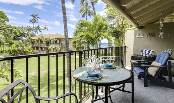 Un balcon avec une table dressée pour deux personnes, des chaises et une vue sur des palmiers et un immeuble.