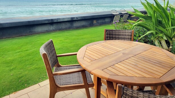 A patio with a wooden table and wicker chairs overlooking a beach.
