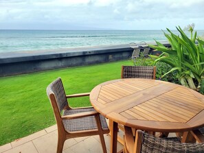 Une terrasse avec une table en bois et des chaises en osier, donnant sur une plage.