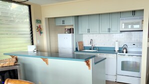 A kitchen with a central island, light blue cabinets, a white refrigerator, a white dishwasher, a white stove, and a wooden chair.