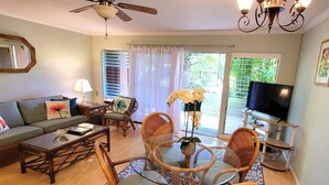 A living room with a sofa, coffee table, dining table with chairs, a TV, and a ceiling fan.