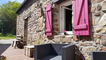 Un edificio de piedra con contraventanas rosas, un banco de madera y una pequeña mesa.