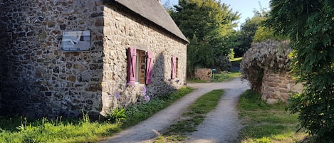 A stone cottage with a thatched roof, a narrow gravel path, and a sign indicating a bed and breakfast.