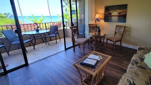 A room with a balcony overlooking the ocean, furnished with a table, chairs, and a sofa. - Ext Maint Special up to 50% disc Ocean Sunset Vw! (Lahaina)