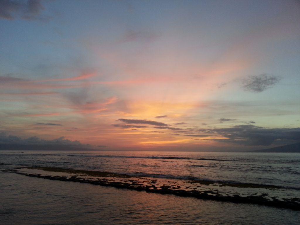 Un atardecer sobre un mar tranquilo con una costa rocosa.