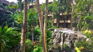 Un jardin luxuriant avec une cascade, des palmiers et un banc.