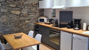 Une cuisine moderne avec un mur en pierre, des armoires blanches, une table à manger en bois et un lave-vaisselle.