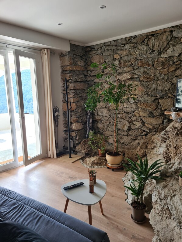 Una sala de estar con pared de piedra, un sofá, una mesa de centro y plantas en macetas.