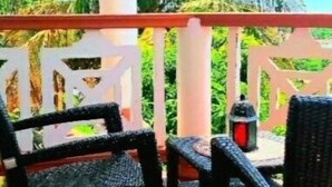 Un balcone con due sedie in vimini e un tavolo, con vista su un giardino tropicale pieno di palme.