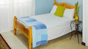 A bedroom with a bed, a bedside table, a window with curtains, and an air conditioning unit. - Samuels Apartment #2 (Kingstown)