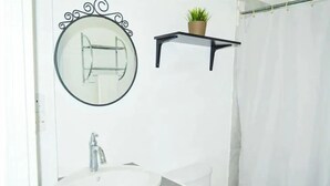 A bathroom with a round mirror, a sink, a toilet, and a shower curtain. - Samuels Apartment #2 (Kingstown)