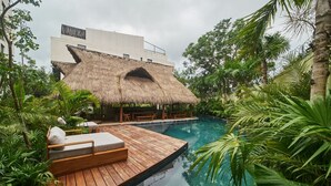 Une piscine dotée d’une terrasse en bois et de chaises longues, entourée d’une végétation tropicale luxuriante.