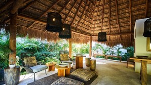 Un espace extérieur aménagé avec des sièges, doté d’un toit de chaume, de mobilier en bois et de luminaires suspendus.
