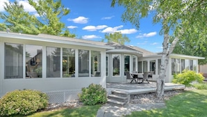 A modern house with large windows, a covered patio, and a well-maintained lawn. - Houghton Lake Getaway w/ Pontoon (Houghton Lake)