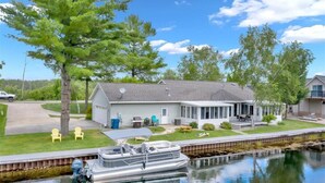 A house with a dock and a boat, surrounded by trees and a clear sky. - Houghton Lake Getaway w/ Pontoon (Houghton Lake)