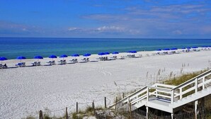 A beach with white sand, blue umbrellas, and lounge chairs.