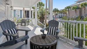 A covered outdoor seating area with Adirondack chairs and a round table, overlooking a palm-lined street.