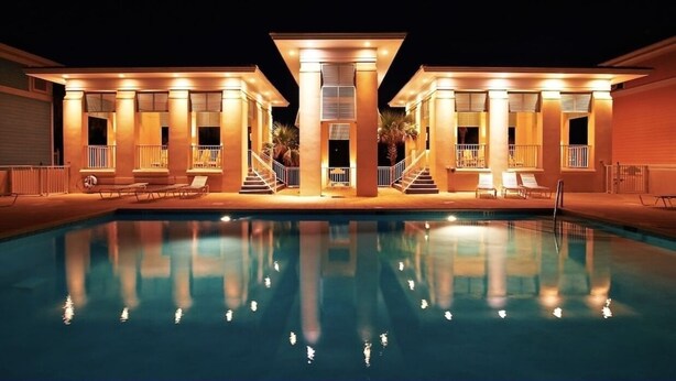 A poolside area with a swimming pool, lounge chairs, and a covered seating area with stairs leading to a balcony.
