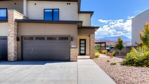 A modern two-story house with a garage, a stone pillar, and a view of mountains in the background. - Luxury twin home.  Beautiful views. Private hot tub. Covered outside patio.  (Moab)
